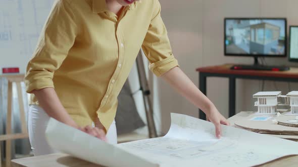 Asian Woman Engineer With A Laptop Looking At Blueprint While Working At The Office