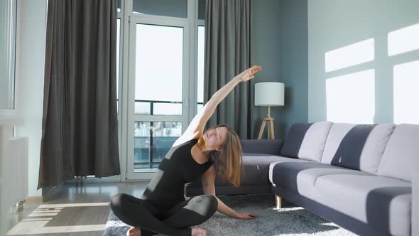 Young Caucasian Woman in Black Jumpsuit Doing Yoga at Home to Develop Flexibility and Balance