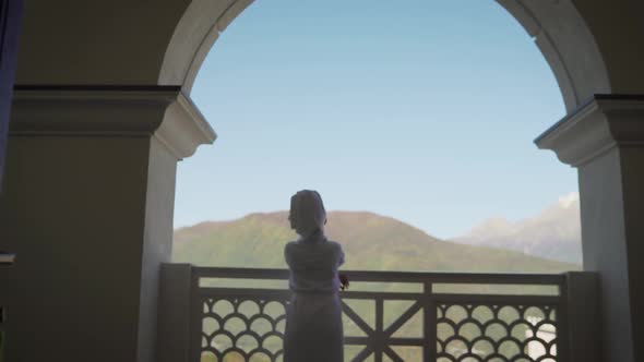 A Girl in a White Robe Stands on the Balcony and Enjoys