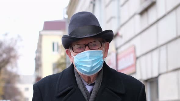 An Old Grandfather in a Protective Mask Walks the Streets of the City