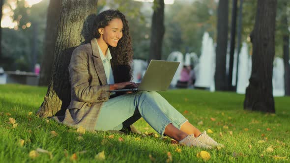 Young Girl Student Successful Business Woman Client User Sitting on Grass Green Lawn in Park City