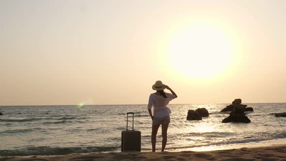 Silhouette of Relaxed Woman with Suitcase on a Sea Beach at Sunset or Sunrise. Travel Concept.