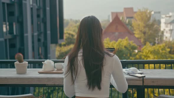 A Young Asian Girl Works at Her Laptop in a Rooftop Cafe in the City