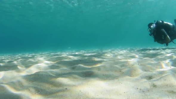 A scuba diver swimming along a sandy beach underwater
