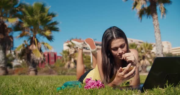 Attractive Woman Laying Down on Park Working with Computer Using Mobile Phone