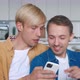 Two Men Homosexual Couple Sit at Home Together in an Embrace on Their Sofa and Using Smartphone - VideoHive Item for Sale