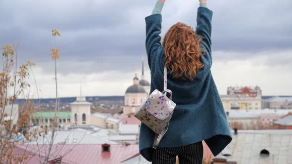 Young Redhaired Woman in a Blue Coat and Walks Against the Backdrop of the Old City