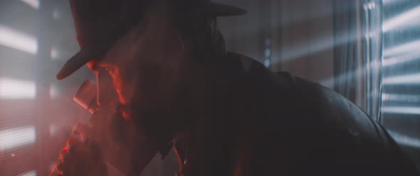 Man wearing hat recording with vintage camera in smoke and red lights