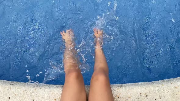Child Splashing Feet in Swimming Pool Water