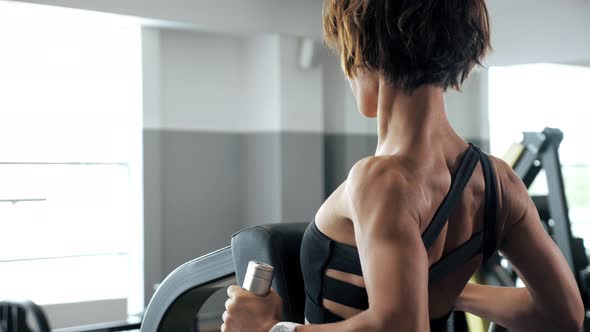 Woman Is Making Exercises for Spine Muscles on Rowing Machine, Back View