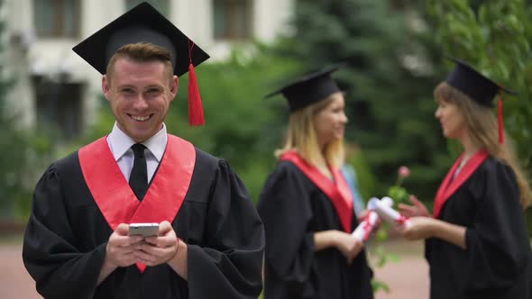 Smiling Male Graduate Holding Smartphone and Looking Into Camera Graduation