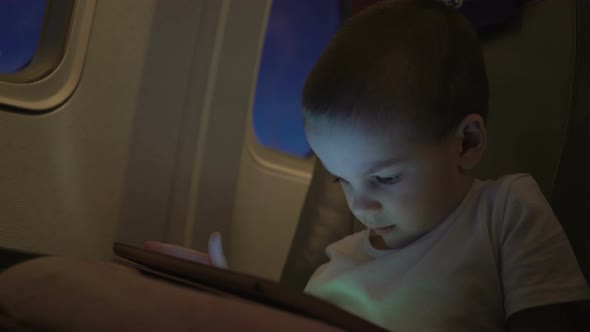 Cute Boy Traveling in an Airplane and Playing with a Computer Tablet