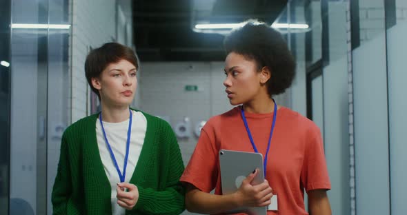 A Young Women with Badges Talking As They Walk Through the Corridor in Office