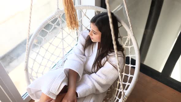 Sexy Brunette in White Bathrobe on a Hanging Chair