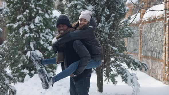 Medium Shot of Joyful African American Father Holding Daughter on Back Looking at Camera Smiling