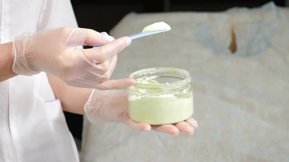 Female Beautician Picks Up Cream with Spatula