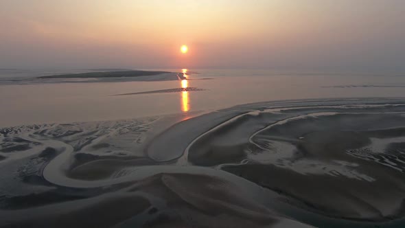 Aerial, rising, drone shot overlooking scenic patterns on a beach, towards sunset