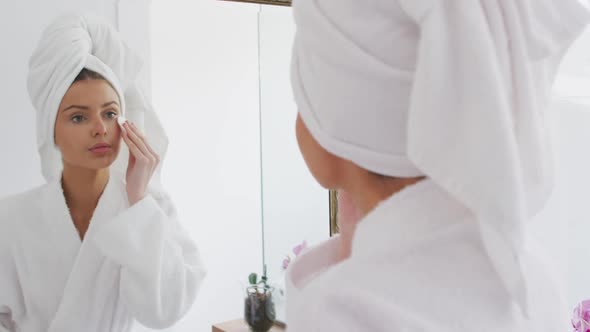 Woman in bathrobe removing make up with cotton pad while looking in the mirror