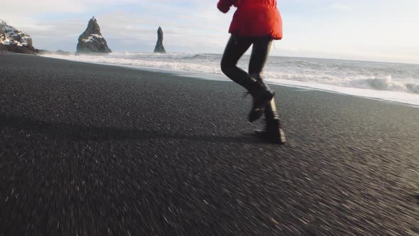 Traveler Woman in a Red Jacket Running on Volcanic Black Sand Beach in Iceland