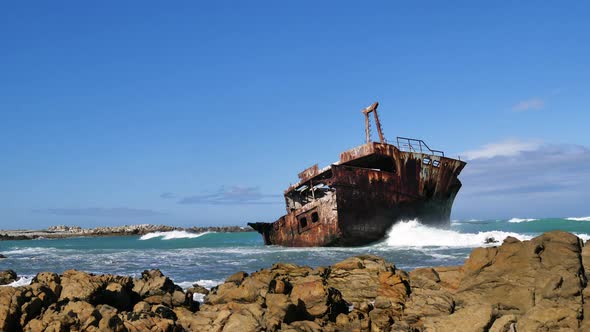 TimeLapse - Rusted old half-shipwreck lying next to rocky coastline of L'Agulhas, waves running in,