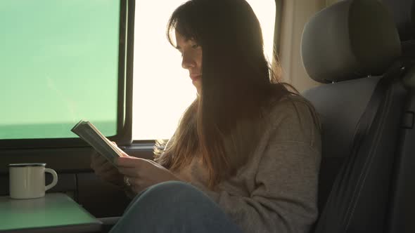 Traveling woman reading book in van at sunset