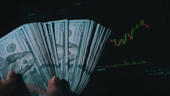 Stack of Dollars in a Hand on the Background of a Stock Market Chart