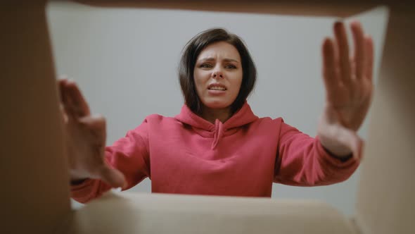 View inside the box on Disappointed brunette woman in red hoodie open delivery internet shopping box