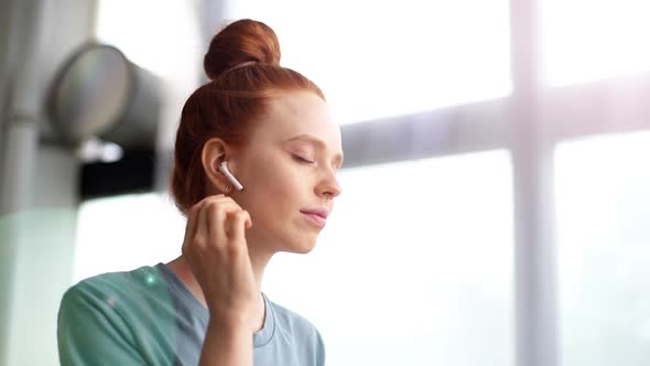 Close-up of Face of Redhead Young Woman Listening Music in Wireless Earphones.