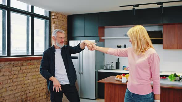 Mature Couple Graybearded Man and Beautiful Blonde Dancing in the Kitchen at Home