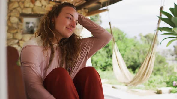 Smiling caucasian woman sitting and relaxing on sunny cottage terrace, looking to garden