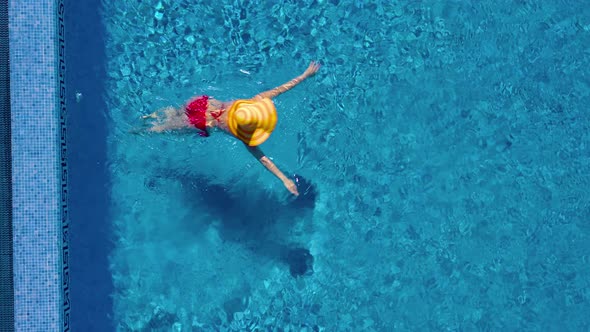 View From the Top As a Woman in a Red Swimsuit and a Big Yellow Hat Swims in the Pool