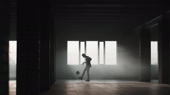 A Black Man Makes a Football Freestyle with a Ball in an Underground Parking Lot in the Sunlight