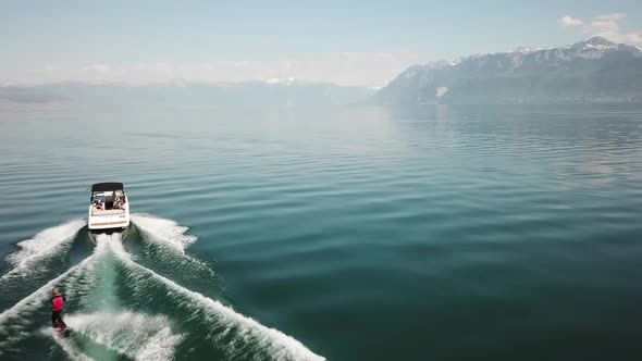 A wakeboarder is behind a motorized boat on Lake Geneva at midday in summer, top down drone view, Sw