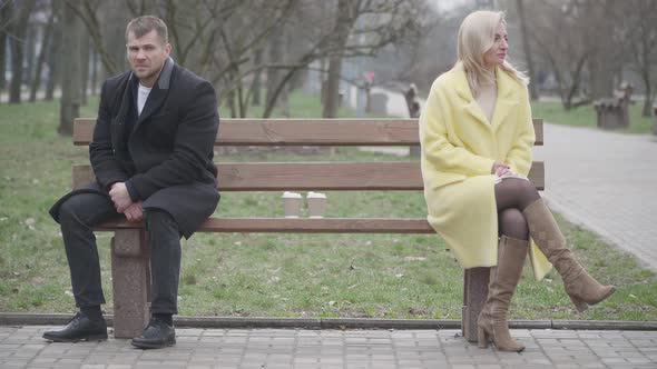 Wide Shot of Argued Caucasian Couple Sitting on Opposite Sides of Bench in Park and Looking Away