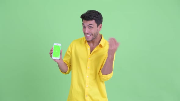 Happy Young Hispanic Businessman Showing Phone and Giving Thumbs Up