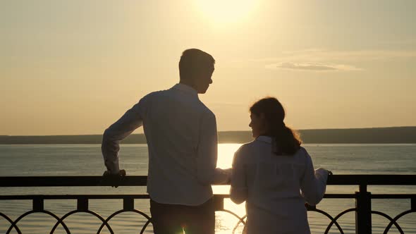 Young Disabled Couple Looks at River at Back Sunset Light