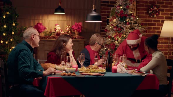 Festive Man Disguised As Santa Claus Giving Family Members Gifts While Enjoying Christmas Dinner