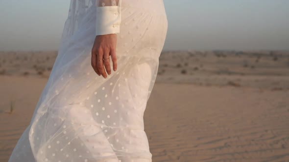 A Woman in a White Dress Barefoot is Walking Along the Desert Sand