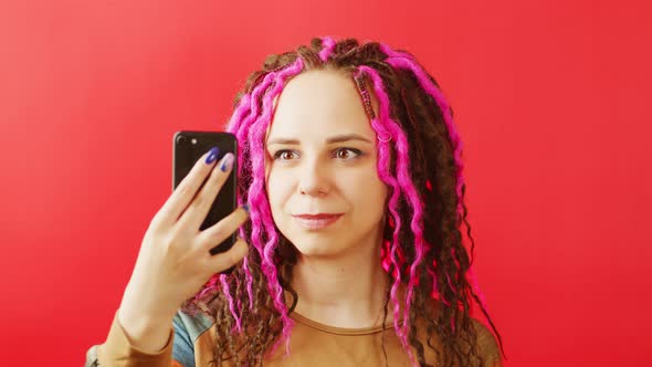 Young Woman with Mobile Phone Takes Selfie on Red Background