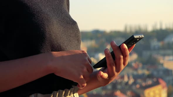 Young Black Woman Works on Smartphone - Buildings in the Background - Closeup