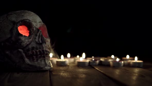 Skull with Glowing Red Eyes That Emit Smoke Against Background of Candles.