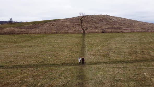 Two Men Stand in a Field at the Crossroads Against the Backdrop of a Mountain