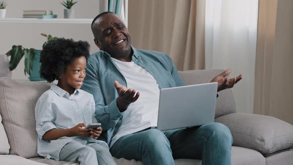 Upset Male Freelancer Sitting on Sofa in Room with Laptop Dissatisfied with Result Loses Online Game