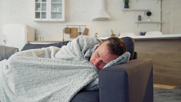 Sick man under warm blanket on comfortable couch at home.