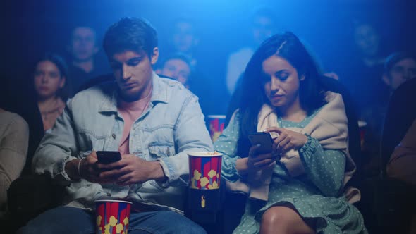 Upset Man and Frustrated Woman Looking in Cellphones in Movie Theater.