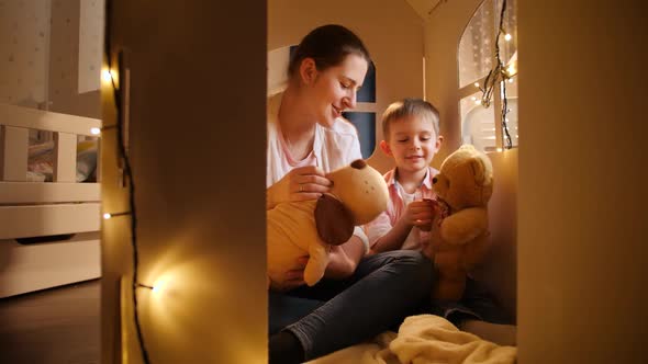 Cute Little Boy and Young Mother Playing Games with Toy Teddy Bears at Night in Tent or Toy House