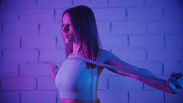 Young Woman Exercising in Neon Lighting Using an Elastic Band to Train Her Hands Against the Brick