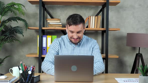 Smiling teacher man sitting on chair at desk in home open and start using laptop