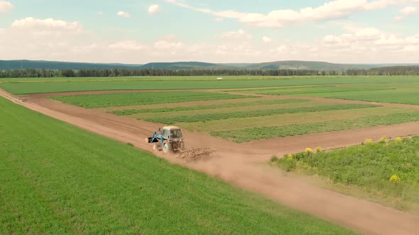 Drone Flying Over Field and Blue Cultivation Tractor Driving on a Ground Road.