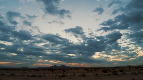 Storm clouds passing over Mojave Desert at orange and blue sunrise, TIMELAPSE